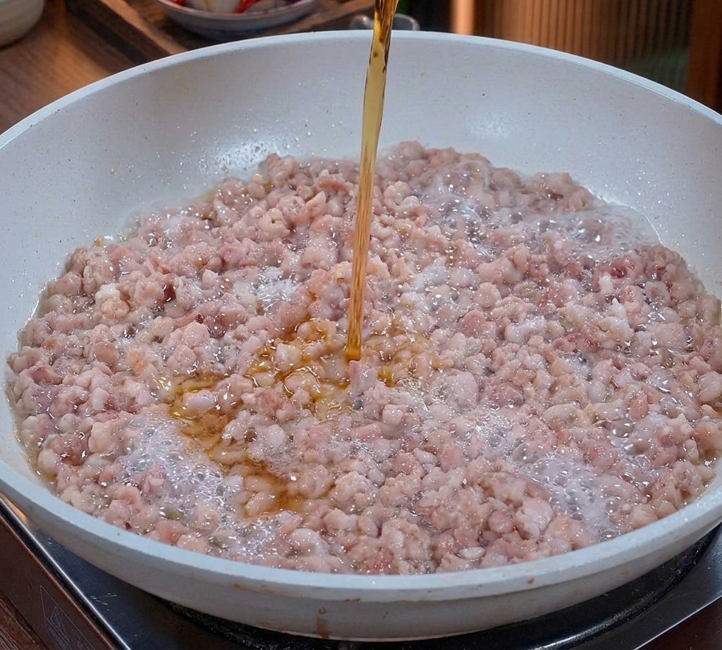フライパンで炒めている豚ひき肉に、グラスから注がれる透明な琥珀色の液体