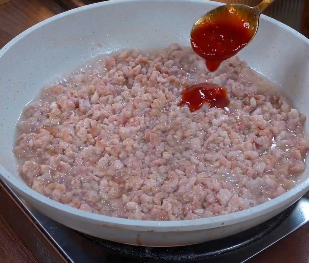 フライパンで炒めたひき肉に、金属製のスプーンから注がれるとろみのある濃い茶色のソース