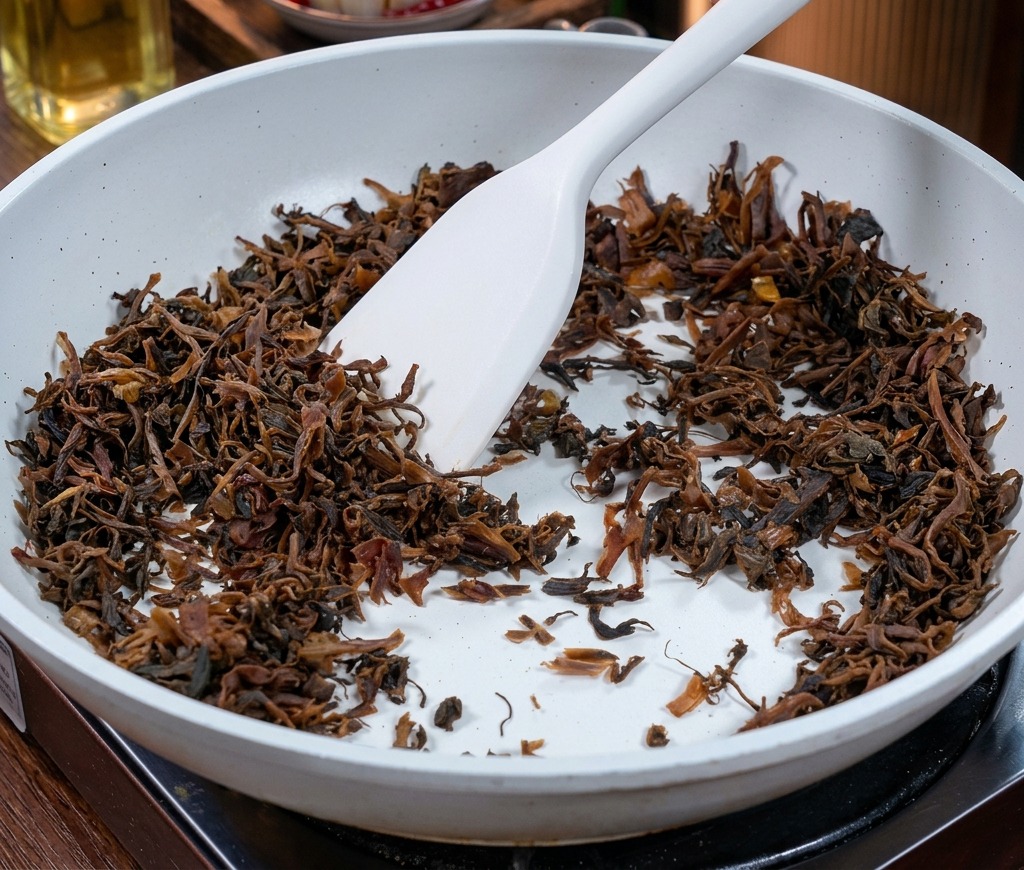 白いセラミックコーティングのフライパンの中で、白いヘラを使って炒められている濃い茶色の刻みヤーツァイ