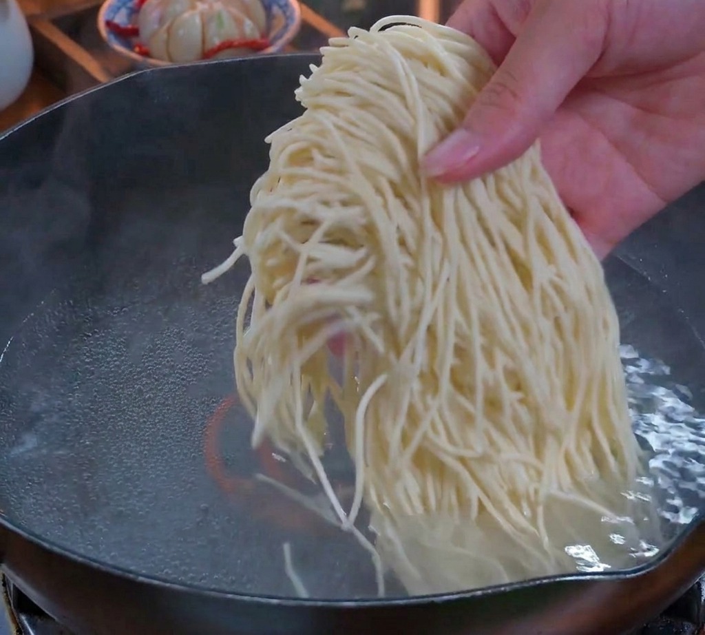 グラグラと沸騰したお湯の入った鍋に、生の中華細麺の束を投入する手