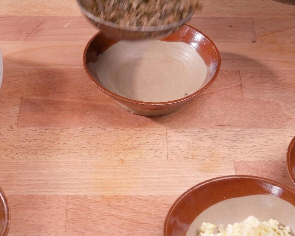 お玉を使って、炒めた豚肉と芽菜のそぼろを木の上の陶器のボウルに移している様子。