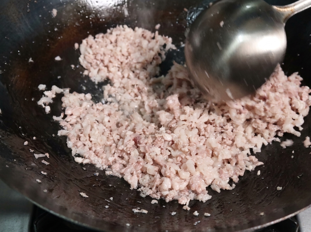 熱い中華鍋の中で、お玉を使って豚ひき肉を炒め、肉の色が変わって細かくほぐれ始めている様子。