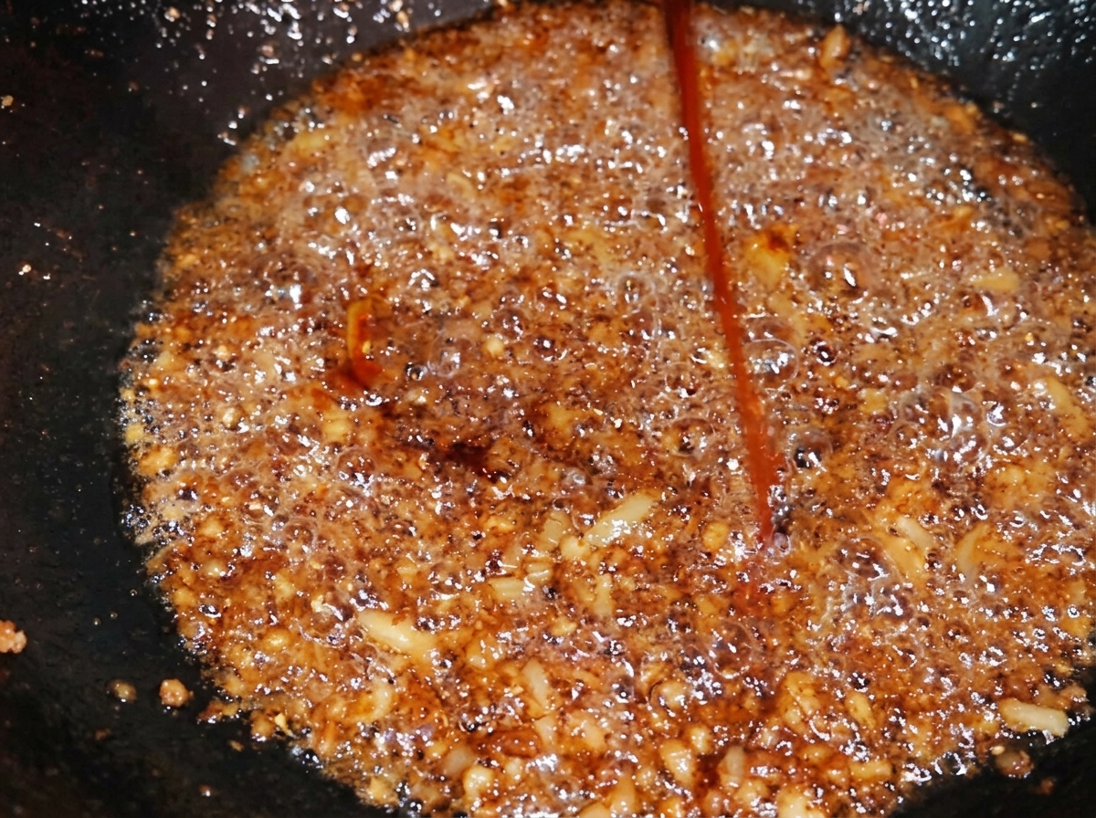味付けした豚ひき肉に濃いキャラメル色の調味料を回しかけ、全体のトーンを深みのある色に変化させている様子。