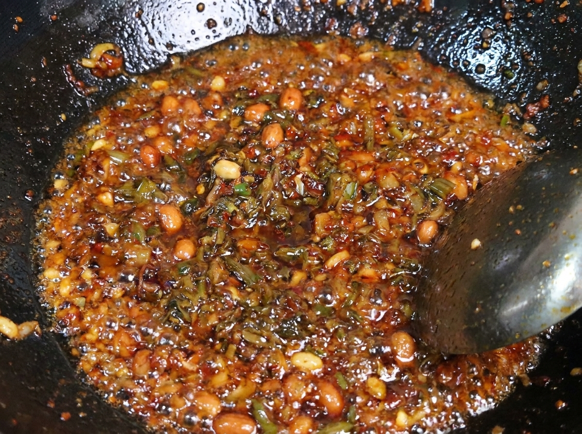 熱い金属製の中華鍋の中で、味付けした豚ひき肉と色の濃い宜賓芽菜を一緒に炒め合わせている様子。