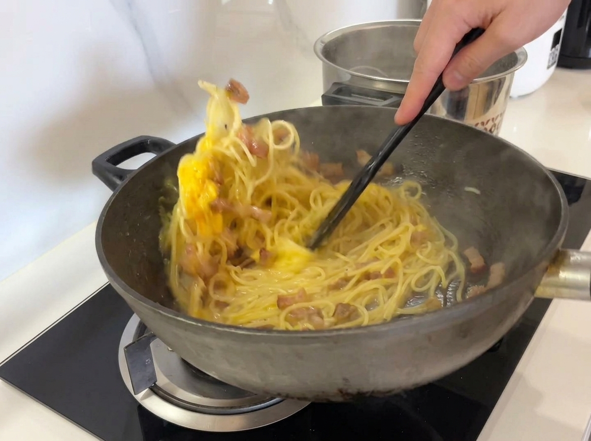 ヘラを使い、パスタ、グアンチャーレ、卵液を力強く混ぜ合わせる様子。
