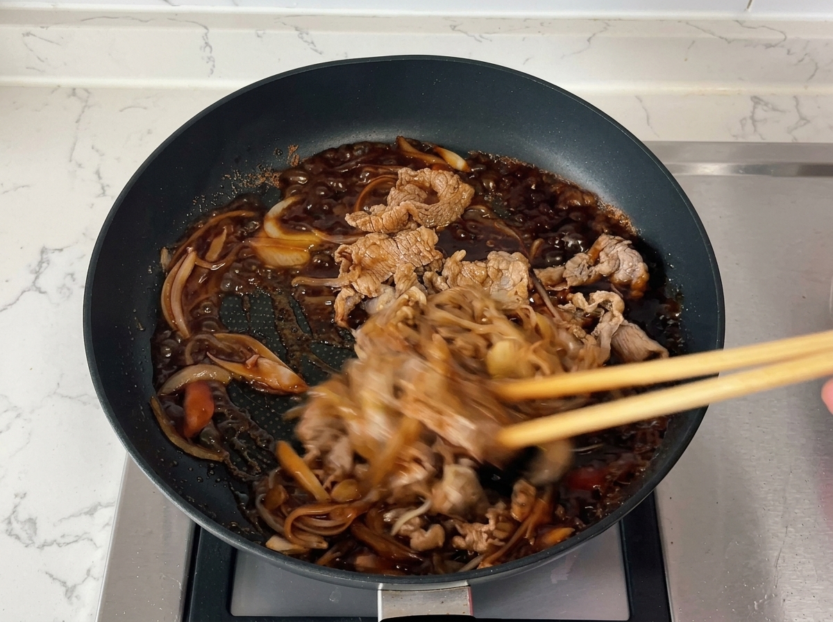 グツグツと泡立ちながらとろみのついた濃いタレの中で、牛肉と玉ねぎを箸で素早く混ぜ合わせている様子。
