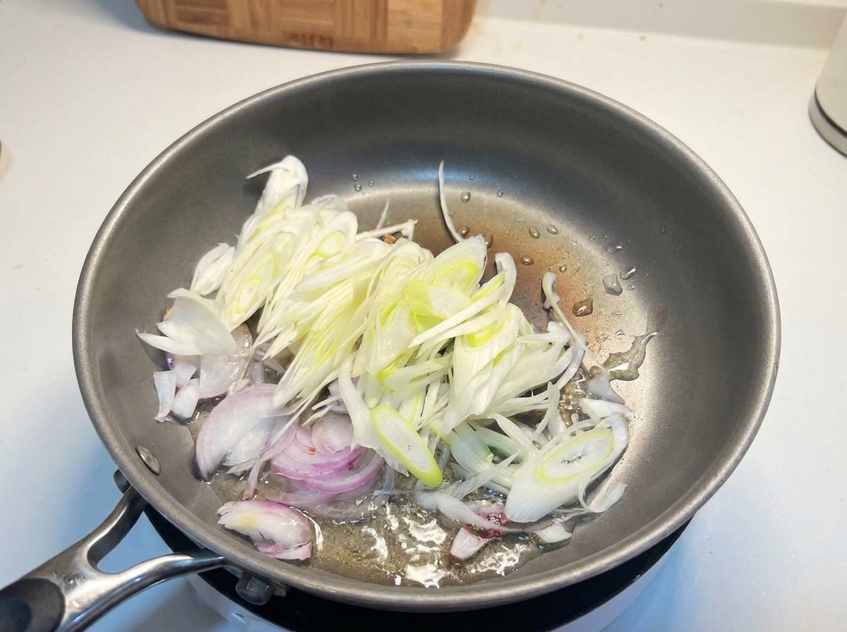 熱したフライパンで、薄切りにした玉ねぎと長ねぎを炒めている様子。