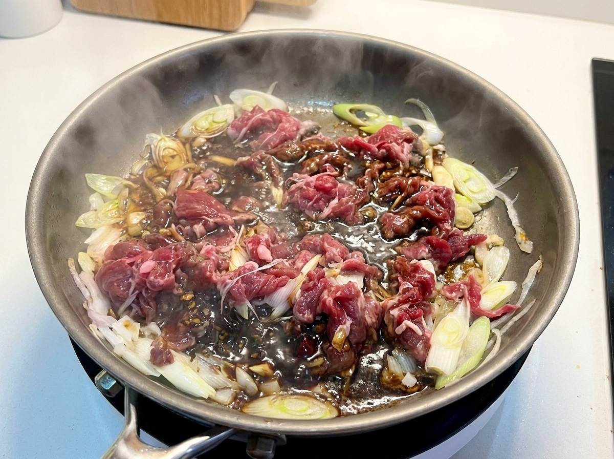 フライパンの中の牛肉と玉ねぎに、濃厚な合わせ調味料を注ぎ入れている様子。