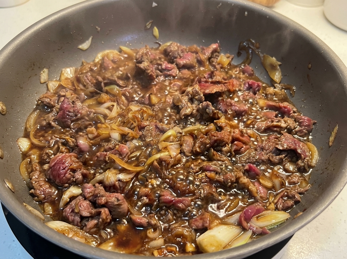 フライパンの中で、茶色く色付いた牛薄切り肉がタレと共に勢いよく煮つまっている様子。