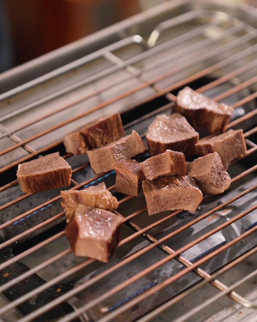 焼き網の上の厚切り牛タンに、ハケを使って濃厚な濃い茶色の照り焼きダレをたっぷりと塗っている光景。