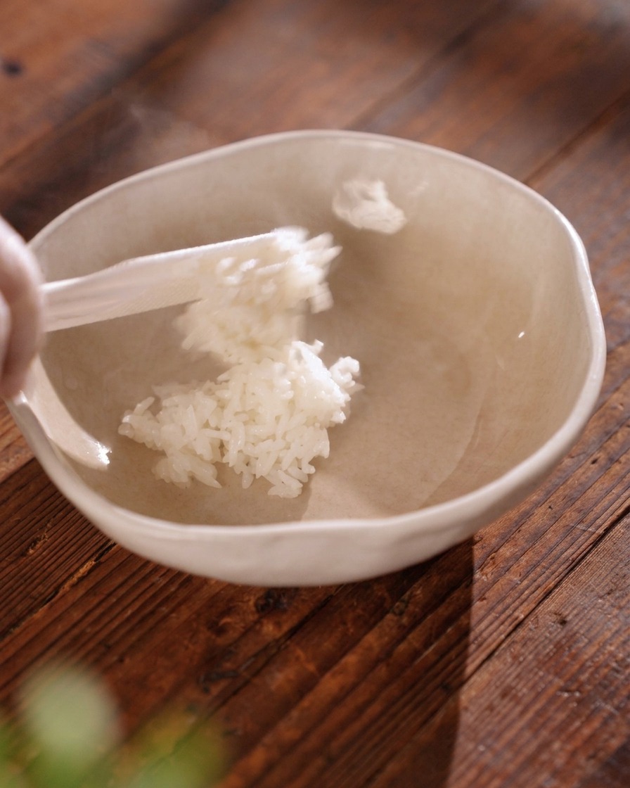 ベージュのセラミック製の丼に、白いしゃもじを使って湯気が立つふっくらとした白米をよそっている様子。