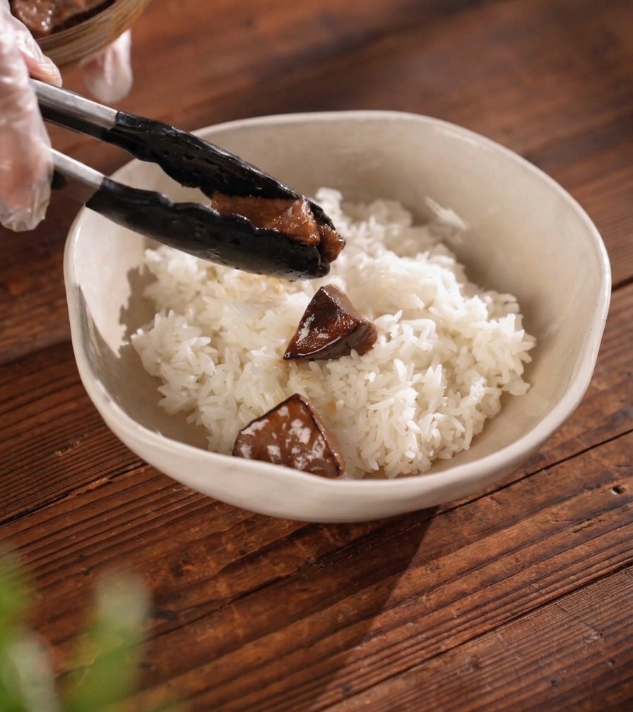 丼に盛られた白いご飯の上に、トングを使ってツヤよく焼き上がった濃い色の牛タンをバランスよく乗せている様子。