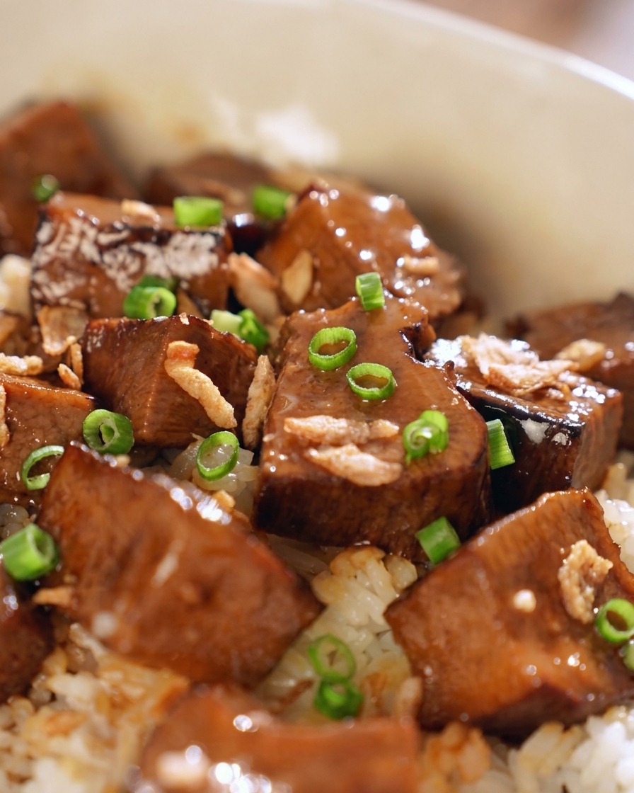 タレが絡んだ牛タン丼の上に、鮮やかな緑色の刻み青ネギときつね色のフライドシャロットを散らしているクローズアップ。