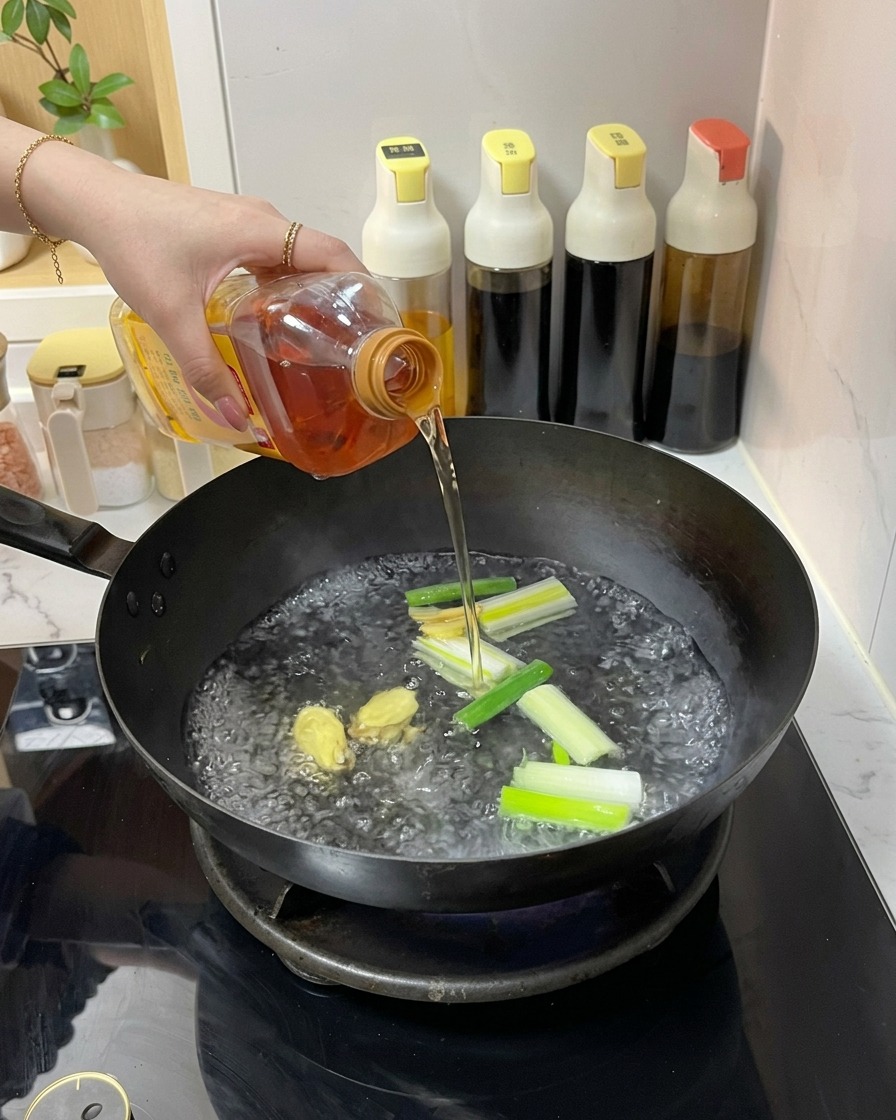 沸騰したお湯、生姜、長ねぎが入った中華鍋に、プラスチックのボトルから透明な琥珀色の液体を注いでいる様子。