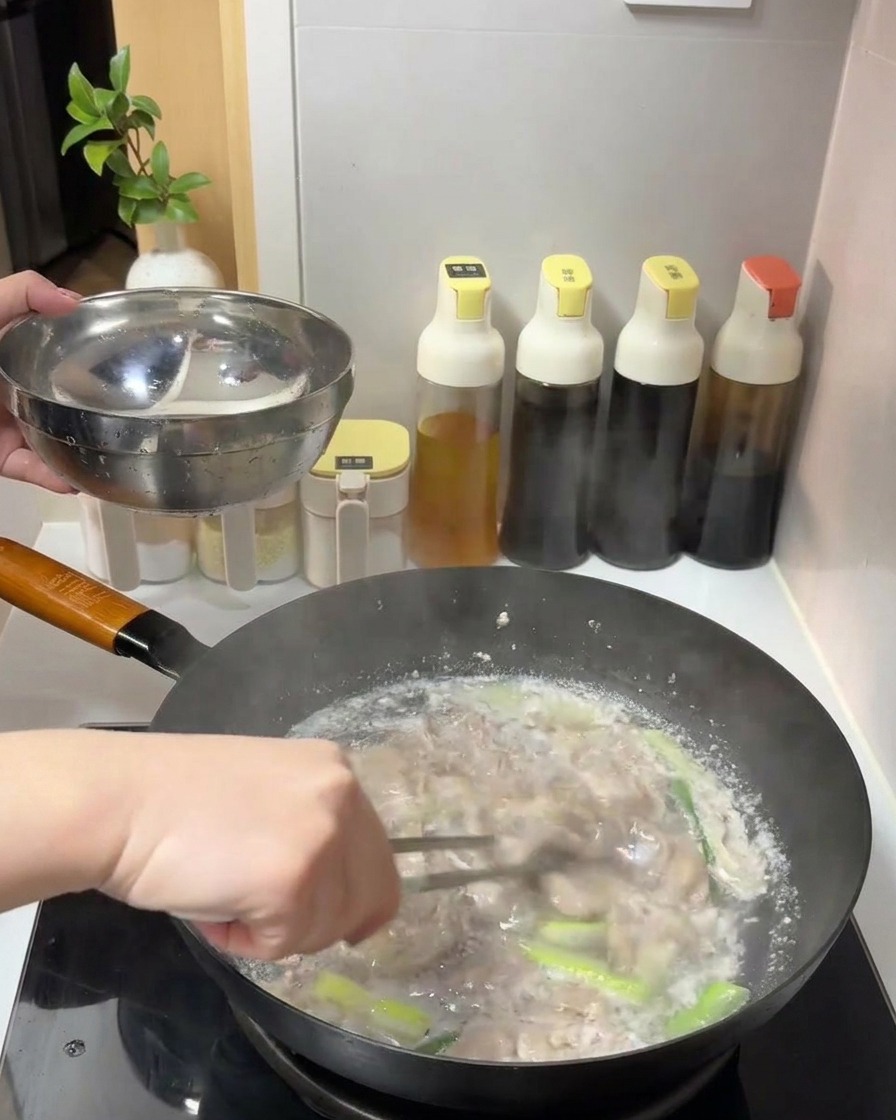 トングを使って、茹だったお湯から火の通った牛肉を取り出し、金属製のボウルに移している様子。