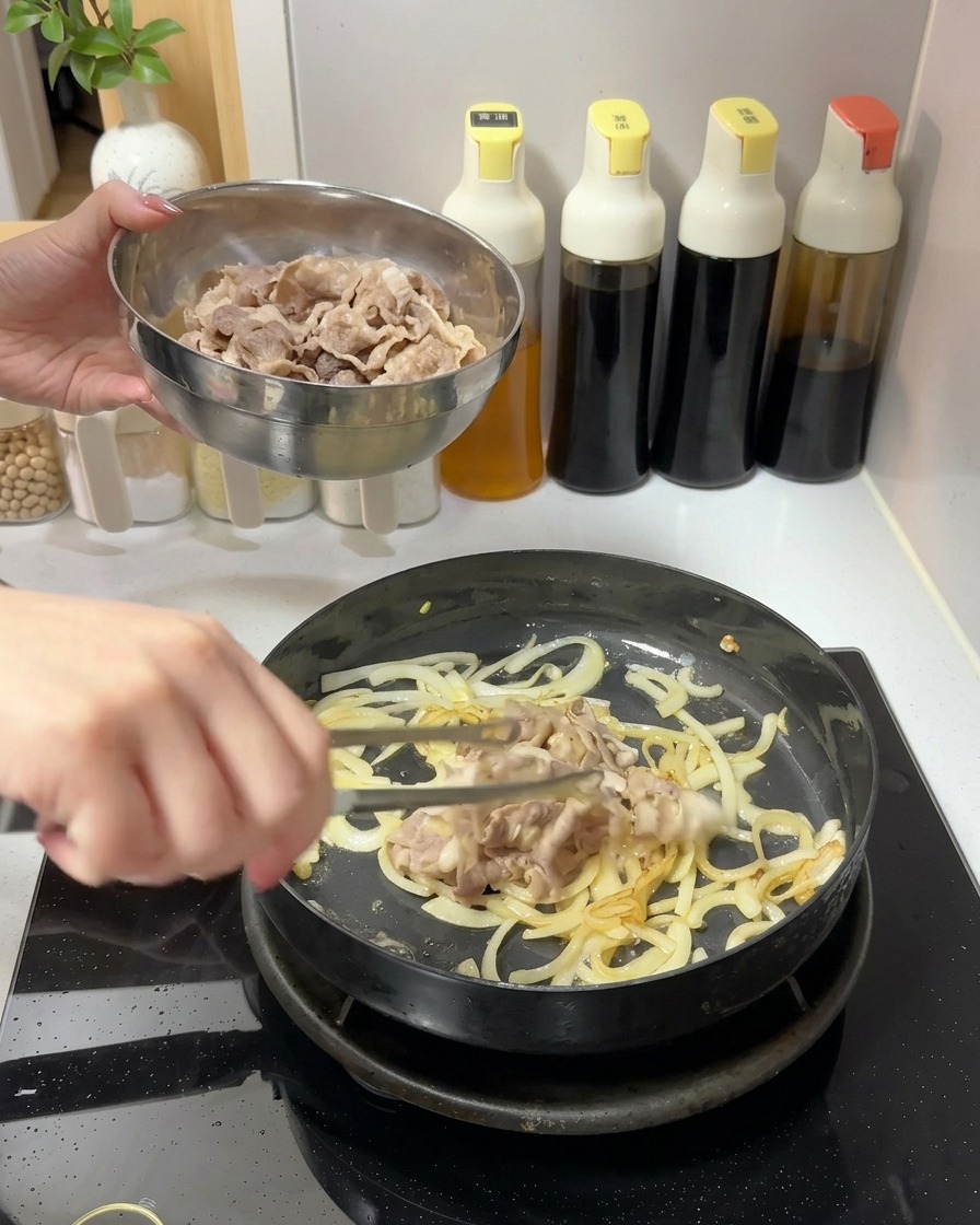 炒めた玉ねぎが入ったフライパンに、ボウルから湯通しした牛肉を加えている様子。
