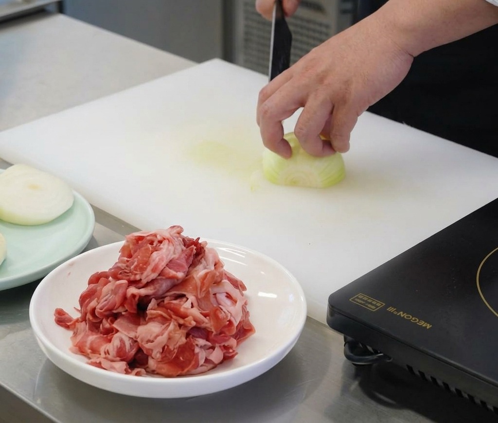 白いまな板の上で、白い玉ねぎを鋭い包丁を使い薄切りにしている料理人の手元。