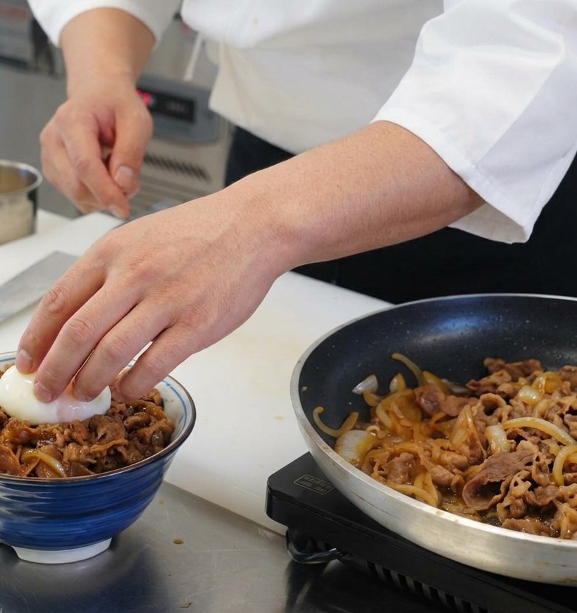 具材がのった丼の中央に、白身が半透明で黄身がとろりとした温泉卵を、手で丁寧にそっと配置している様子。