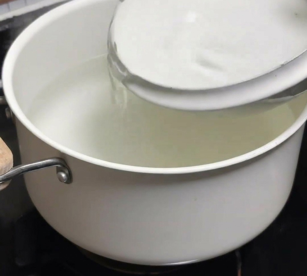 火を止めた熱湯の入った鍋に、器から冷水を注ぎ入れている手元。