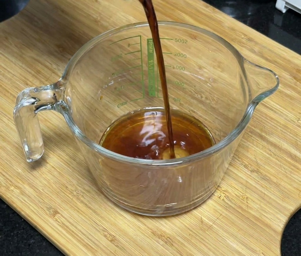 はちみつや調味料が入ったガラスの計量カップに、醤油を注ぎ入れているところ。