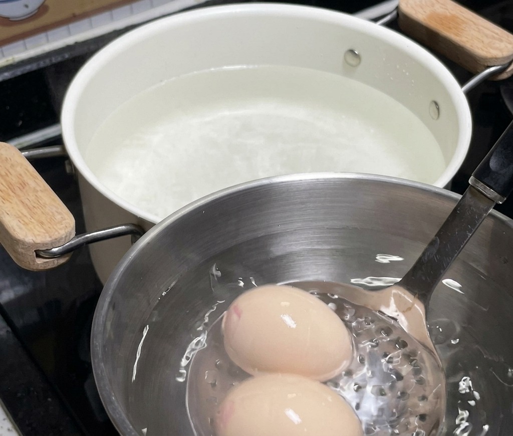 お湯から引き上げた2個の卵を、氷水の入ったステンレス製ボウルに浸して冷ましている様子。