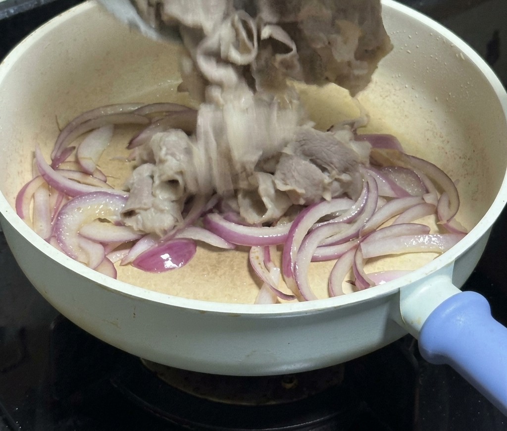 しんなり炒めた赤玉ねぎの入ったフライパンに、ボウルから牛肉を戻し入れている様子。