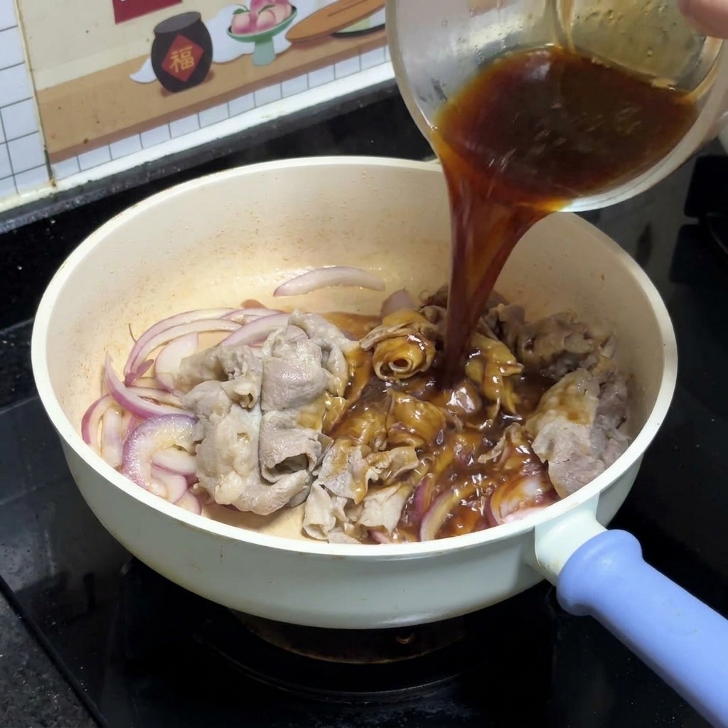 炒めた牛肉と玉ねぎの上に、ガラスボウルから特製の照り焼きダレを回し入れているところ。