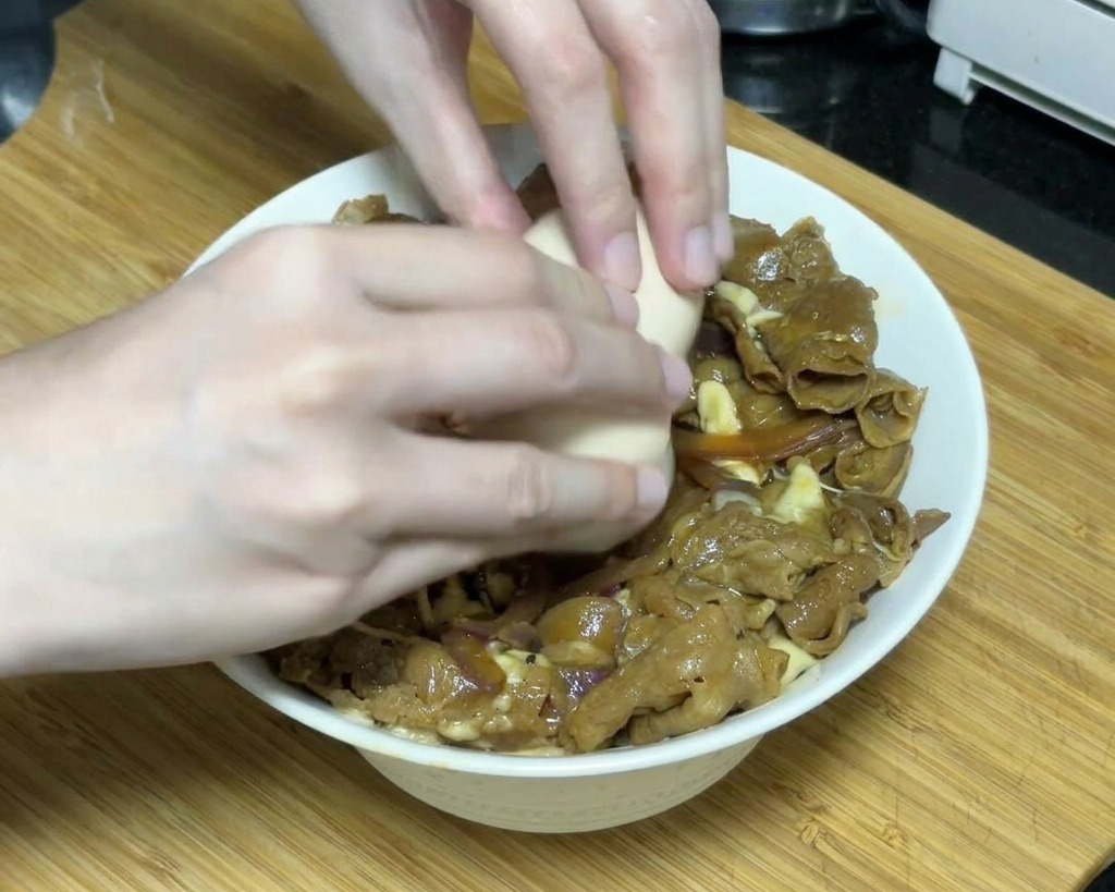 チーズをのせた牛丼の真ん中に、両手でそっと温泉卵を割り落としている瞬間。