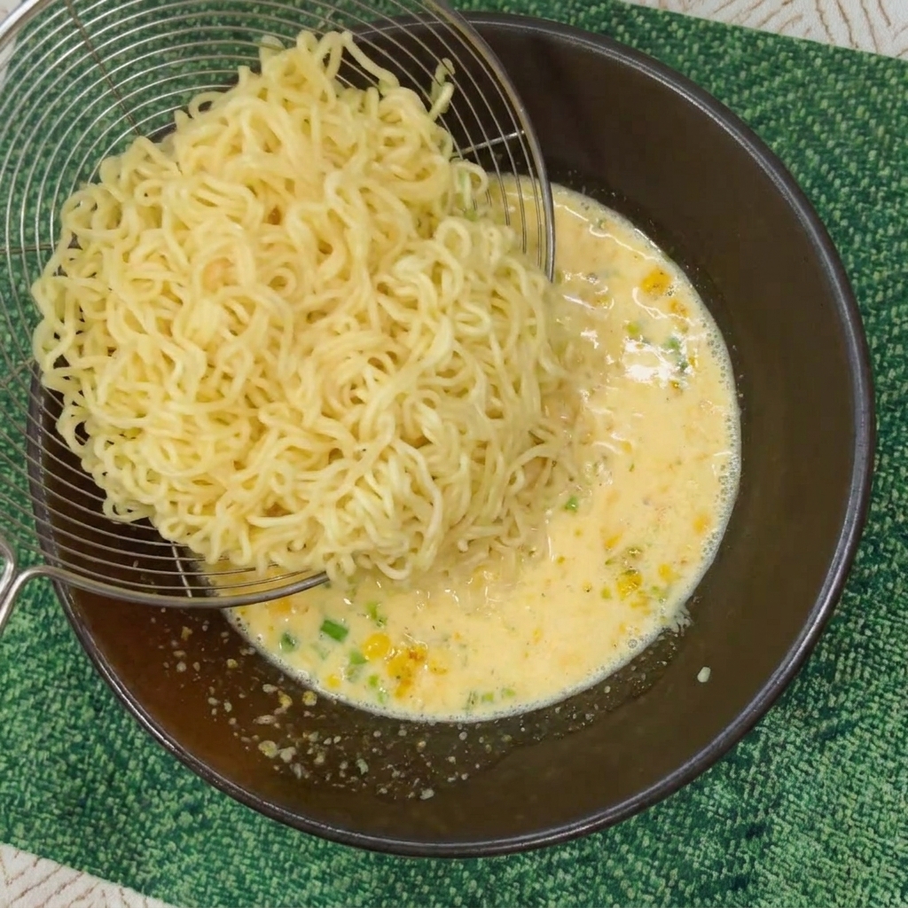 別の鍋で茹でた縮れ麺を、ボウルのクリーミーなスープに移している様子。