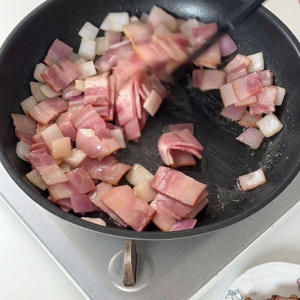 フライパンでベーコンと玉ねぎを炒め合わせ、脂が溶け出している様子。