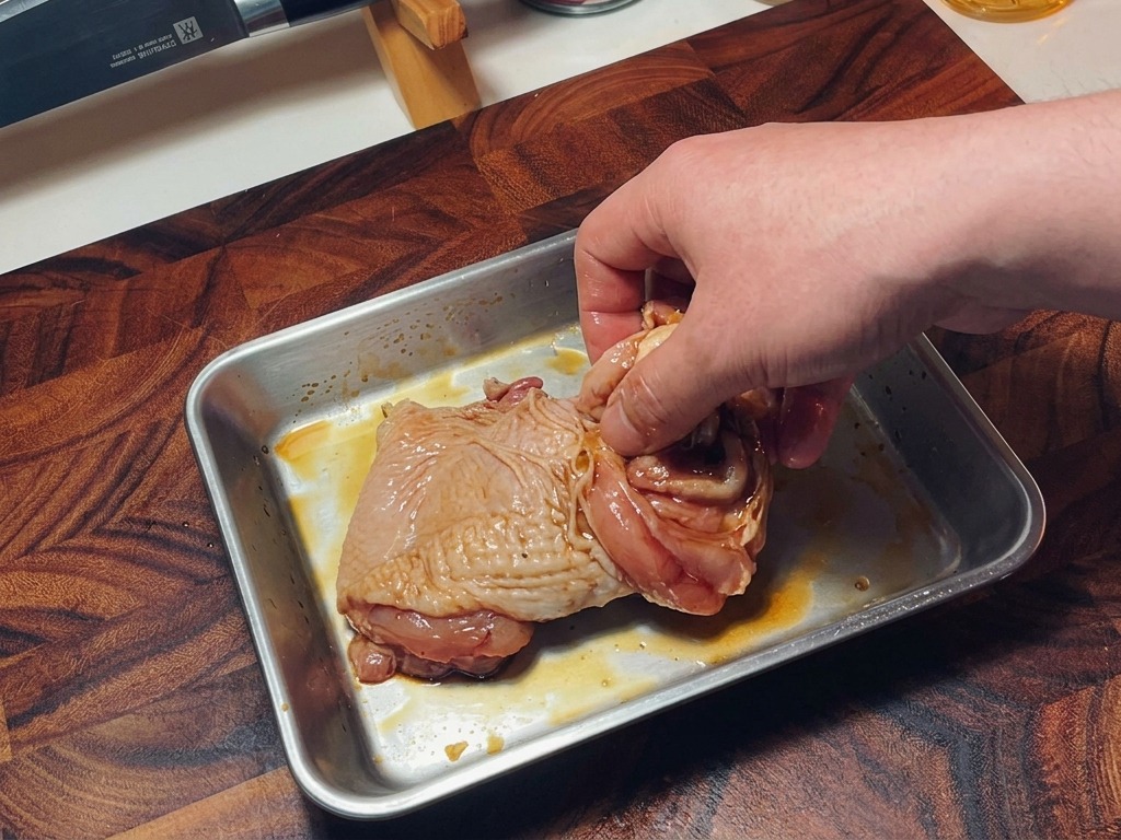 調味料をまぶした生の鶏もも肉を、手でしっかりと揉み込んで全体になじませている様子。