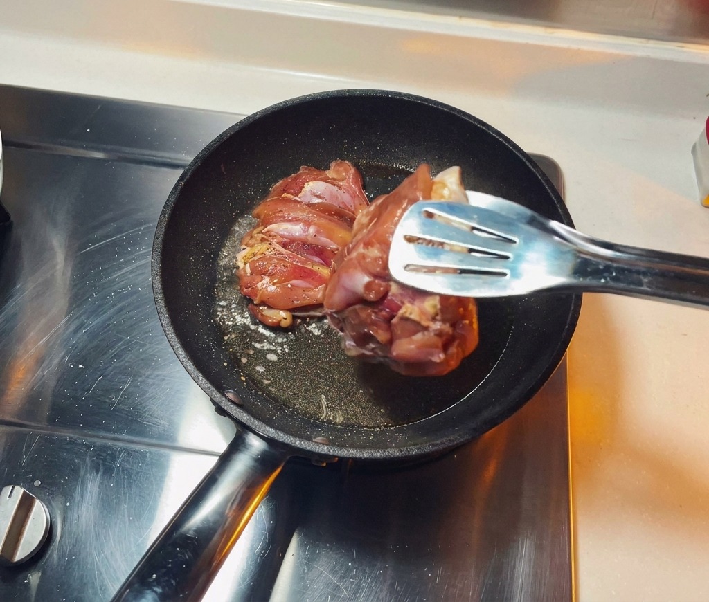 熱したフライパンに油を引き、下味をつけた鶏もも肉を皮目を下にして入れ、じっくりと焼いている様子。