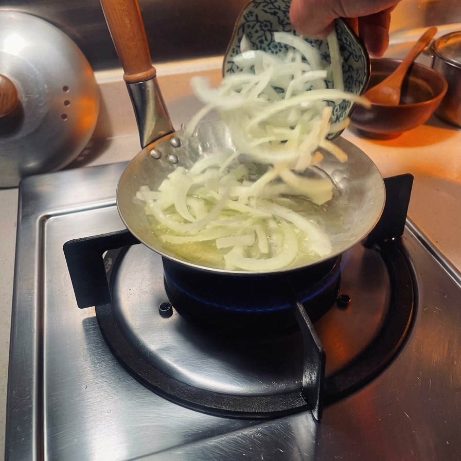 ガスコンロの上の小さな親子丼専用鍋に、スライスした白玉ねぎを入れて炒めている様子。