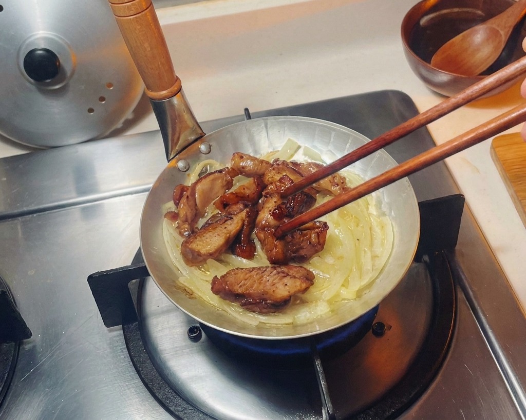 小さなフライパンの中で、しんなりした玉ねぎの層の上に、箸を使って焼き上がった鶏肉を綺麗に並べている様子。