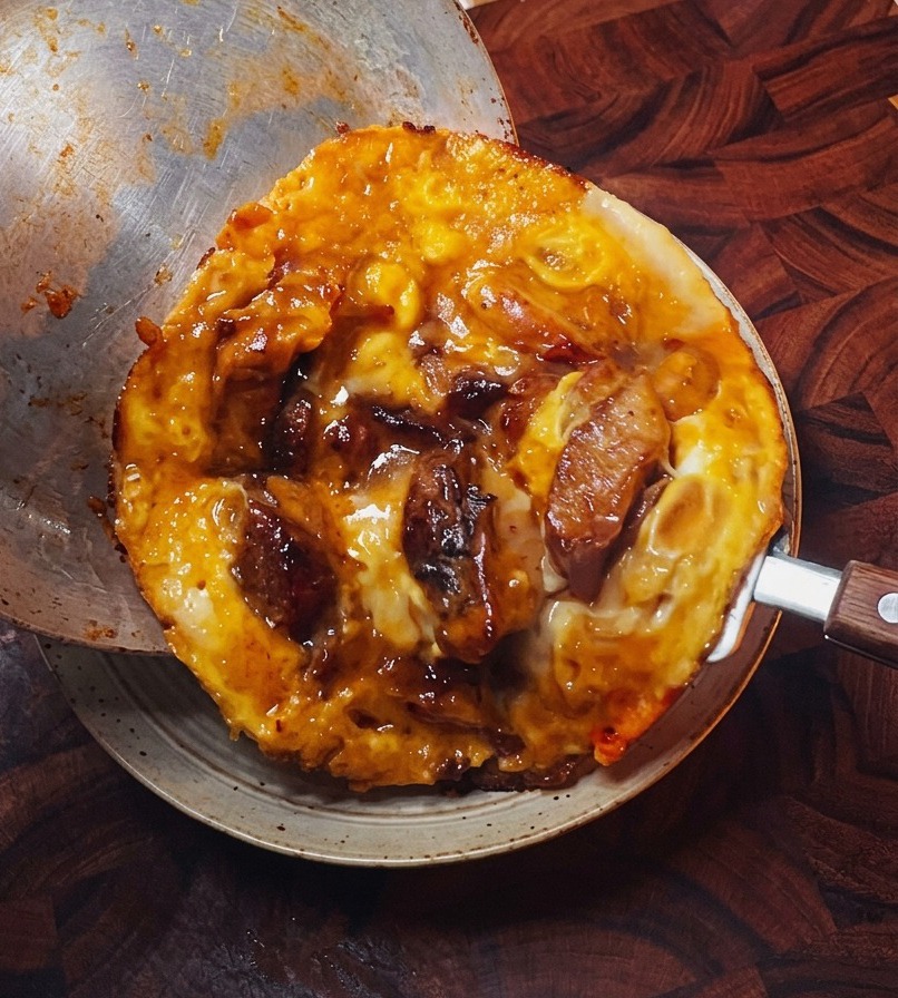 フライパンを傾け、ふんわりと仕上がった卵と鶏肉の具材を、ほかほか白米の入った丼へ滑らせるように移している様子。