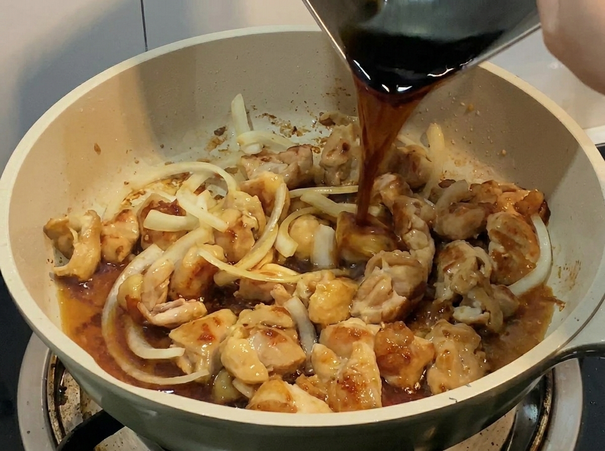 鶏肉と玉ねぎが入ったフライパンに、金属容器から濃い旨味のある液体を直接注ぎ入れている様子。
