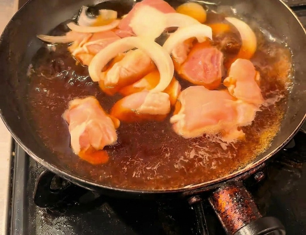 黒いフライパンの中で、醤油ベースのだし汁と一緒にグツグツと煮込まれている鶏肉と薄切り玉ねぎ。