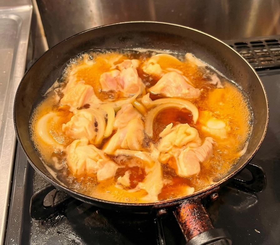 煮立っている鶏肉と玉ねぎの上に、溶き卵を円を描くように優しく注ぎ入れている様子。