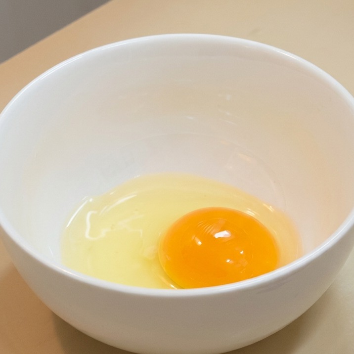 白い陶器のボウルの中に、新鮮な生の卵黄と透明な白身が入っている様子。
