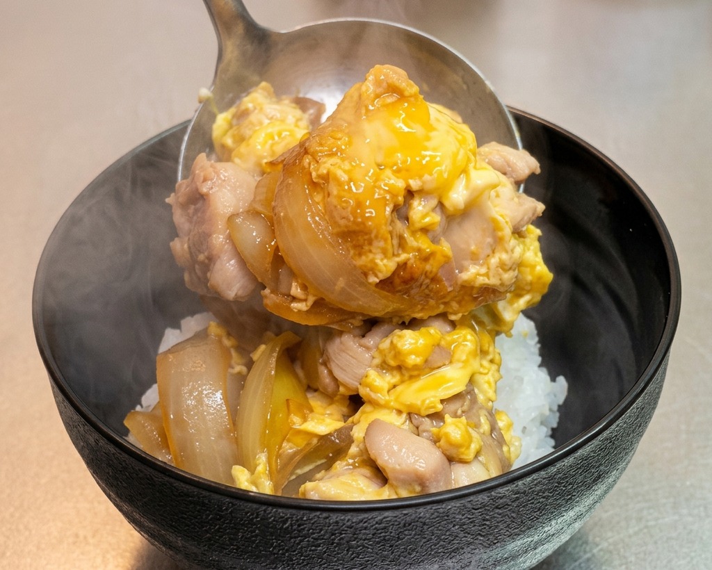 ふっくらと炊き上がった白いご飯の丼に、お玉を使ってアツアツの親子丼の具を盛り付けている様子。