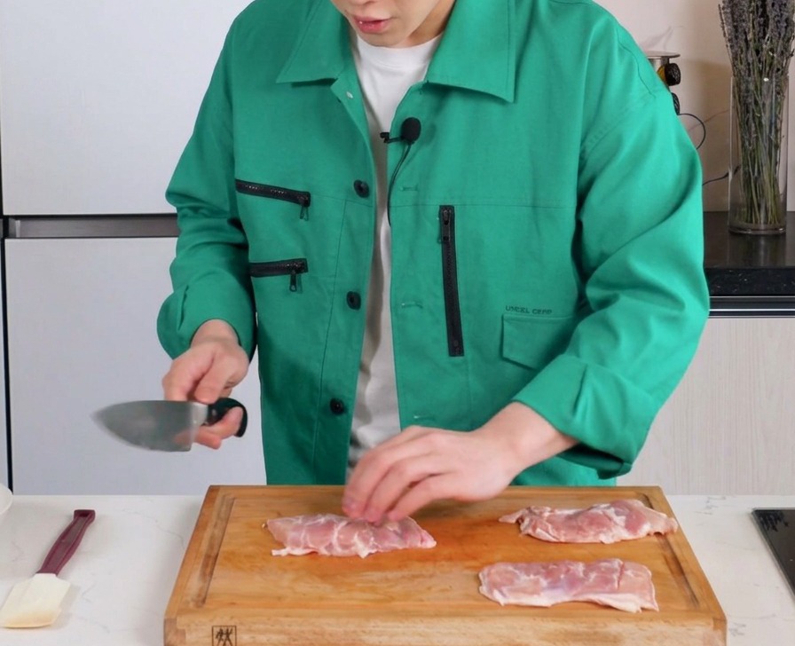 木製のまな板の上で、骨なし鶏もも肉の身の側に包丁で浅い切れ目を入れている様子