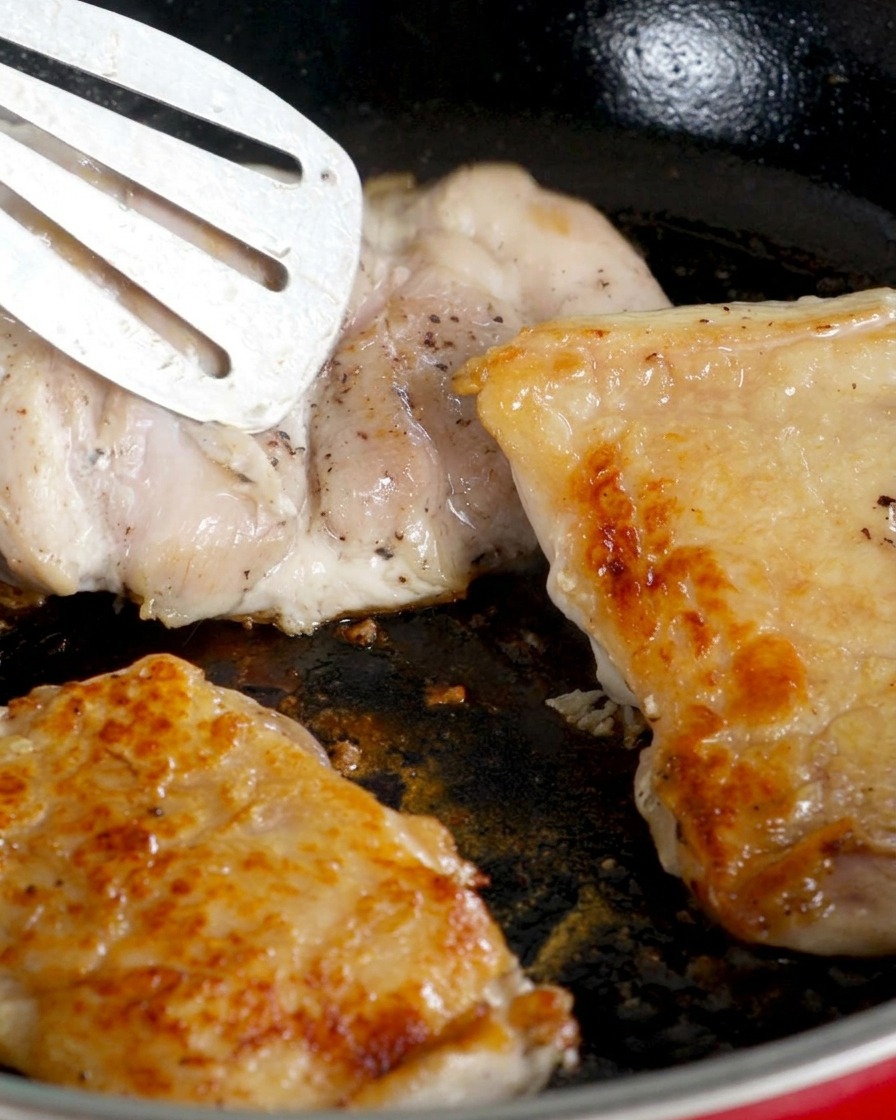 フライパンの中で鶏肉が裏返され、皮目が香ばしく焼けた状態で身の側を焼いている様子