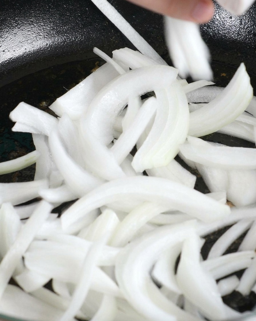 鶏肉の旨味が残ったフライパンに、薄切りにした白玉ねぎを投入している様子