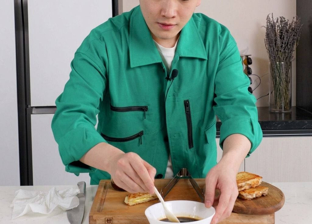 白い小さめのボウルに入った醤油ベースの濃い茶色のタレを、小さなスプーンで混ぜ合わせている様子