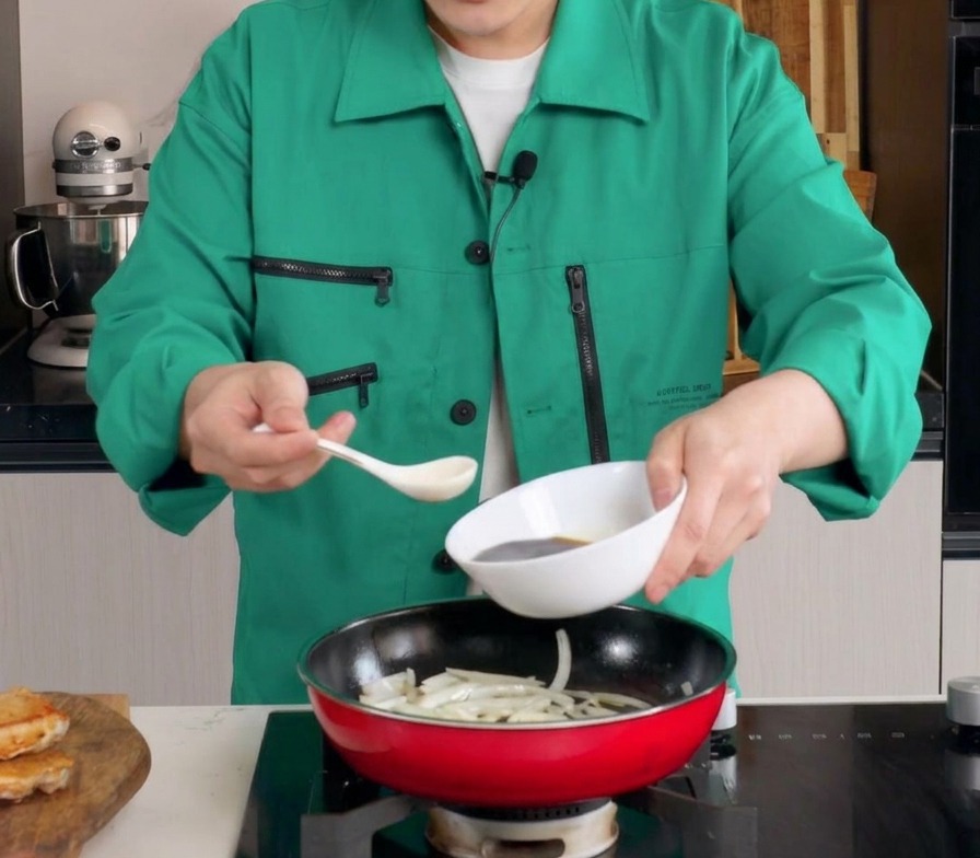 しんなりとした玉ねぎが入った赤いフライパンに、白いボウルから濃い茶色のタレを注ぎ入れている様子