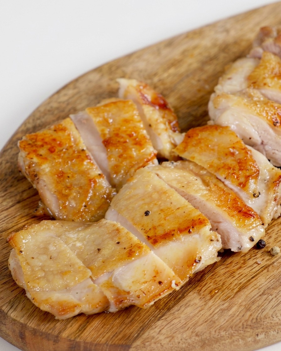 木製のまな板の上で、カリッと焼けた鶏もも肉を均一な大きさに切り分けている様子