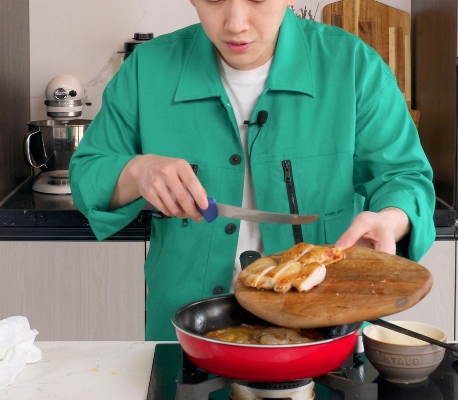 玉ねぎと半熟の卵が入った赤いフライパンに、スライスした鶏もも肉を丁寧に並べている様子