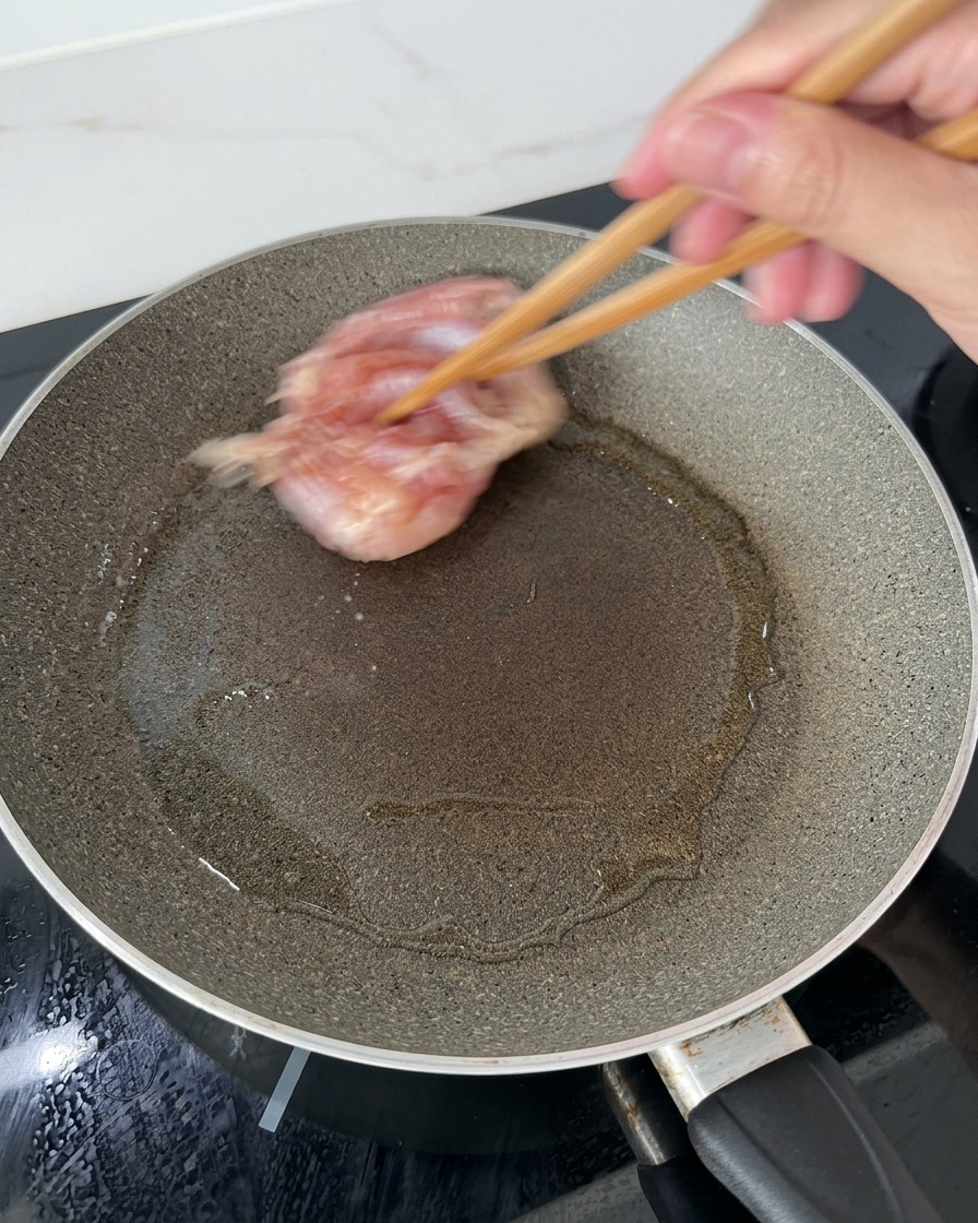 熱したフライパンに油を引き、木箸を使って鶏もも肉の皮目を下にして並べている様子。