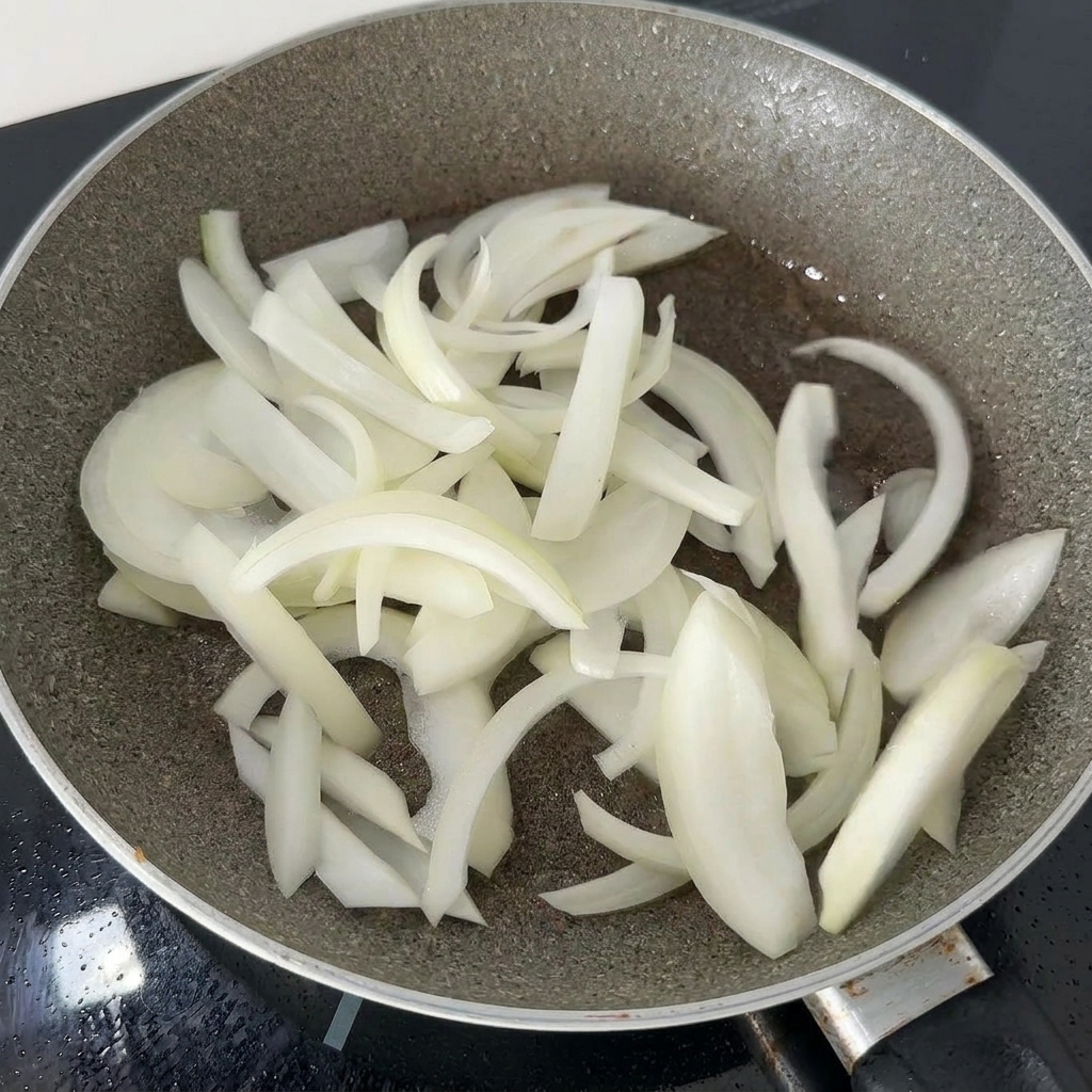 鶏肉の旨味が残ったフライパンの中で、薄切りにした玉ねぎがしんなりするまで炒められている様子。