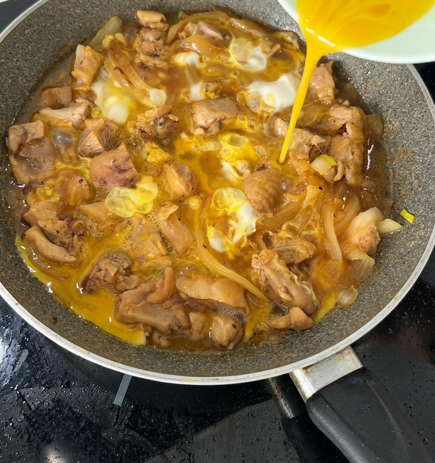 フライパンの中の仕上げ間近の親子丼の上に、残りの半分の卵液を均一に注ぎ入れている様子。
